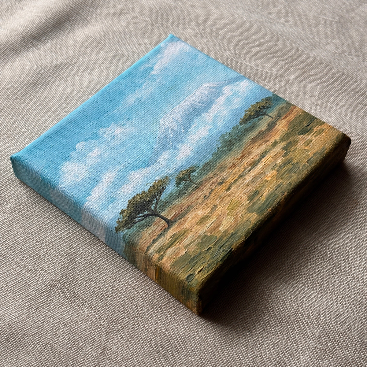 Angled view of a miniature oil painting showing golden grassland and scattered trees beneath a blue sky.
